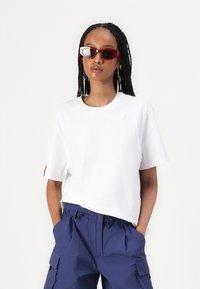 White cotton t-shirt with short sleeves and a round neckline, paired with navy cargo pants. Accessorized with red cat-eye sunglasses.