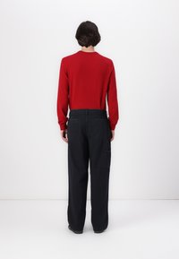 Red knit sweater with long sleeves, paired with loose-fitting black cargo pants featuring side pockets, shown from the back.