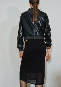 Veste bombardier en cuir noir avec des poignets et un ourlet côtelés, associée à une jupe midi noire avec un panneau inférieur transparent.