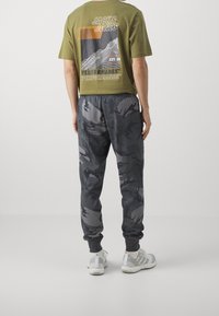 Olivgrön kortärmad T-shirt med bergsgrafik och text, ihop med mörkgrå camouflagebyxor. Vita träningsskor med grå detaljer.