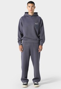 Sudadera con capucha y pantalones a juego en felpa gris oscuro, con un bolsillo en el pecho con marca y detalles en las costuras laterales.