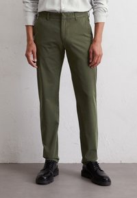 Olive green chinos wykonane z mieszanki bawełny, z prostą nogawką, płaskim przodem i bocznymi kieszeniami, zestawione z czarnymi sznurowanymi butami.