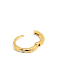 Pulsera de metal en tono dorado con un diseño liso y curvado, y un pequeño acento de piedra clara en un lado. Forma abierta para un ajuste ajustable.