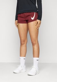Burgundské sportovní šortky s elastickým pasem, se bílým logem. V kombinaci s bílými teniskami a ponožkami s černými akcenty.