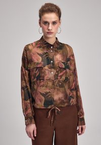 Langærmet skjorte med knapper i transparent stof, der har et flerfarvet blomsterdesign, to brystlommer og justerbart bånd i kanten.