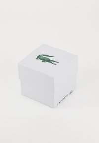 White cardboard box with a textured finish, featuring a green crocodile logo on the top and "LACOSTE" printed on the side.