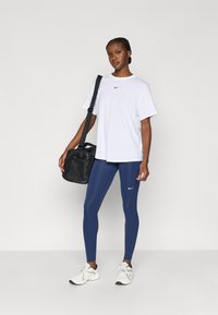 Λευκό κοντομάνικο μπλουζάκι Nike, μπλε ναυτικό κολάν με λογότυπο, μαύρη τσάντα και λευκά sneakers με μαύρες λεπτομέρειες. Λεία υφή υφάσματος και εφαρμοστή σχεδίαση.