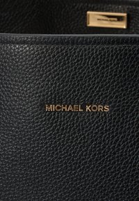 Extérieur en cuir noir grainé avec un logo "MICHAEL KORS" en relief doré. Surface texturée et forme structurée.