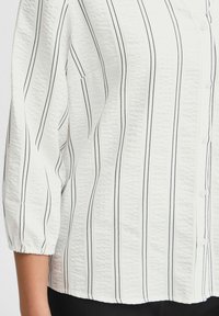 Witte blouse met knoopsluiting en zwarte verticale strepen, met een textuurstof en 3/4-lange mouwen. Kenmerken zijn subtiele knopen en een ontspannen pasvorm.