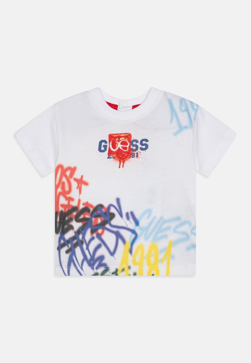 T-shirt bianco a maniche corte con design di graffiti multicolori, incluso il logo "GUESS", con accenti rossi, blu, gialli e neri.