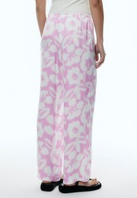 Lichte, wijde broek in een roze en witte bloemenpatroon, met een elastische tailleband en zachte stof. Platte sandalen zichtbaar.