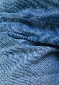 Světle modrá denimová látka se hladkým povrchem a výrazným diagonálním tkaním, s jemnými záhyby a vráskami.