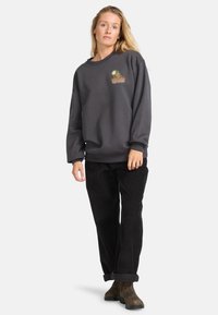 Donkergrijze oversized sweatshirt met een ronde halslijn en een subtiele meerkleurige grafische logo op de borst, gecombineerd met zwarte corduroybroek.