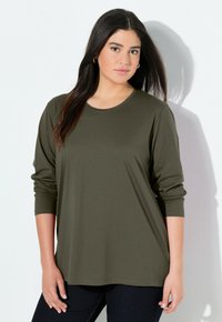 T-shirt à manches longues de couleur vert olive en tissu doux, avec un col rond et une coupe décontractée, associé à un jean foncé. Design simple.