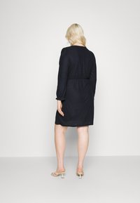 Vestido azul-marinho, até ao joelho, com tecido texturizado, mangas longas bufantes e cintura ajustada. Material leve e detalhe de padrão subtil.