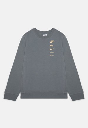 Sweatshirt Nike gris à manches longues avec petits logos et texte dorés indiquant "NIKE", "SWOOSH" et "JUST DO IT." sur la partie supérieure gauche de la poitrine.