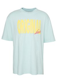 Vaaleansininen puuvillapaita rennolla leikkauksella. Edessä on "ORIGINAL" paksulla keltaisella tekstillä ja vaaleanpunainen "Levi's" -logoyksityiskohta.