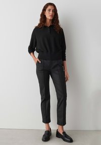 Sweatshirt nera a maglia con colletto henley, abbinata a pantaloni neri su misura con texture liscia e vestibilità slim. Indossato con mocassini neri.