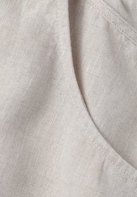 Gaišbeigā lina audums ar gludu tekstūru, ar izliekto malu un smalkiem piešuvuma elementiem.