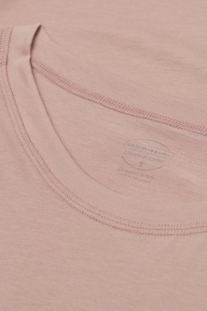 Nahaufnahme des Halsausschnitts eines blassrosa Baumwoll-T-Shirts mit doppelt genähten Nähten und einem schwach gedruckten Größenetikett innen.