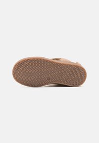 Brown rubber shoe outsole with a diamond pattern. Soft, suede upper visible at the top edge, designed for traction and comfort.