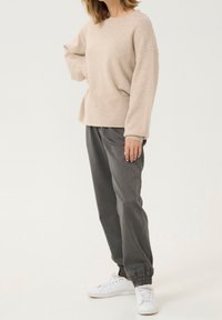 Beige Wollpullover mit langen Ärmeln und lässiger Passform, kombiniert mit dunkelgrauen Jogginghosen mit elastischen Bündchen und weißen Sneakers.