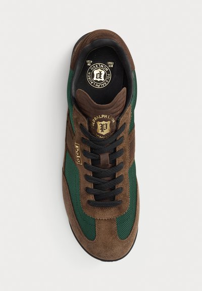 Brown suede sneaker with green mesh panels, black laces, and gold branding accents. Rounded toe and padded collar, flat rubber outsole.