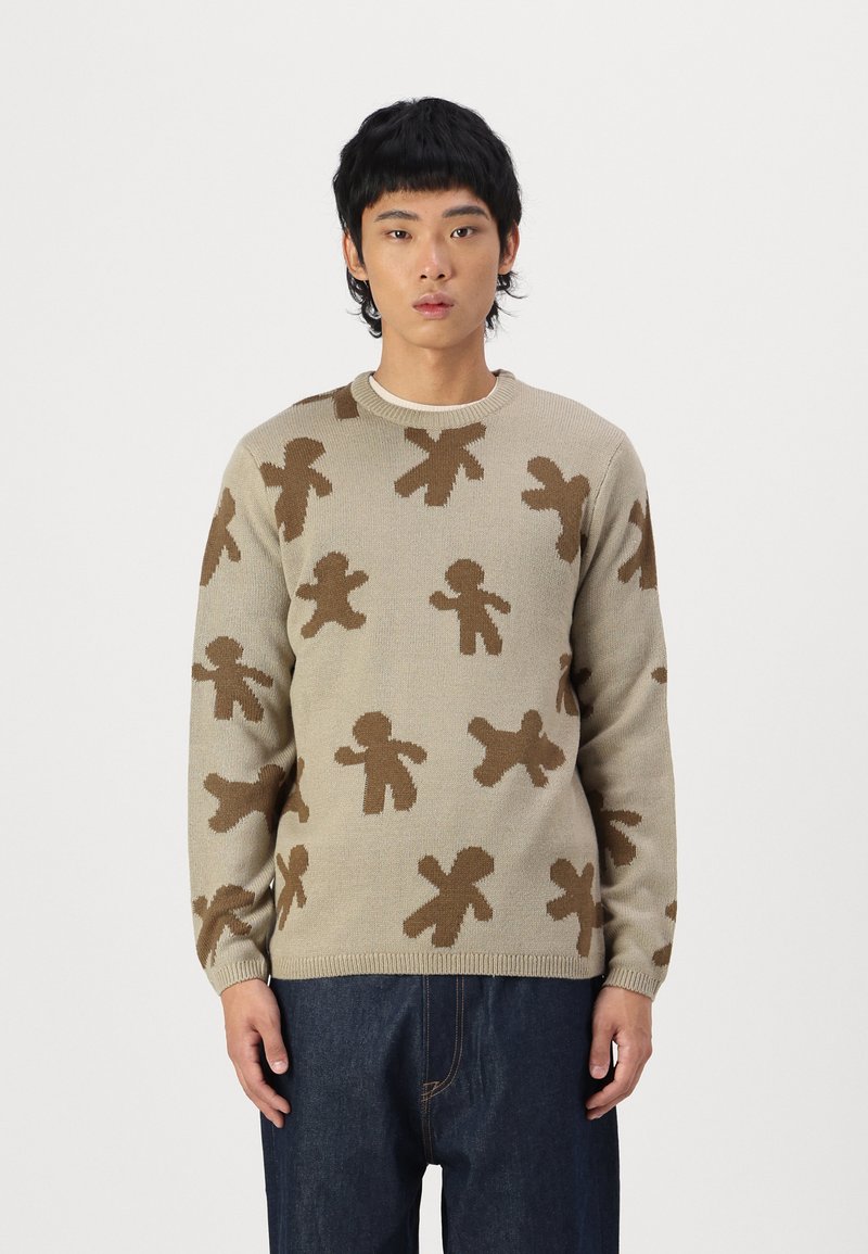 Beige sweater with a knit pattern of brown gingerbread figures. Crew neck and ribbed cuffs. Worn with dark denim pants.