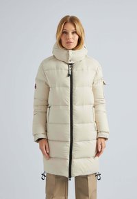 Doudoune beige avec un col haut, dotée d'une fermeture éclair sur le devant, de poches latérales et de cordons de réglage à l'ourlet. Texture lisse et matelassée.