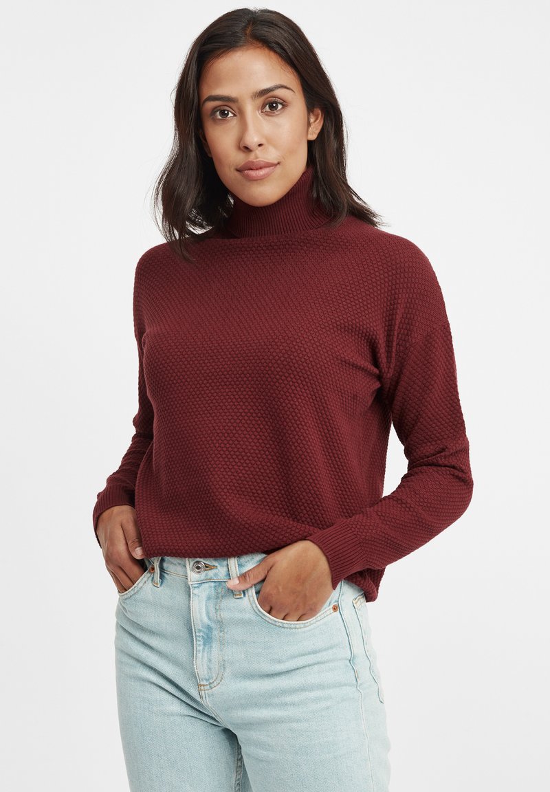 Bordeaux coltrui met een gemêleerd, patroon gebreide ontwerp, met lange mouwen en een losse pasvorm, gecombineerd met lichtblauwe jeans.