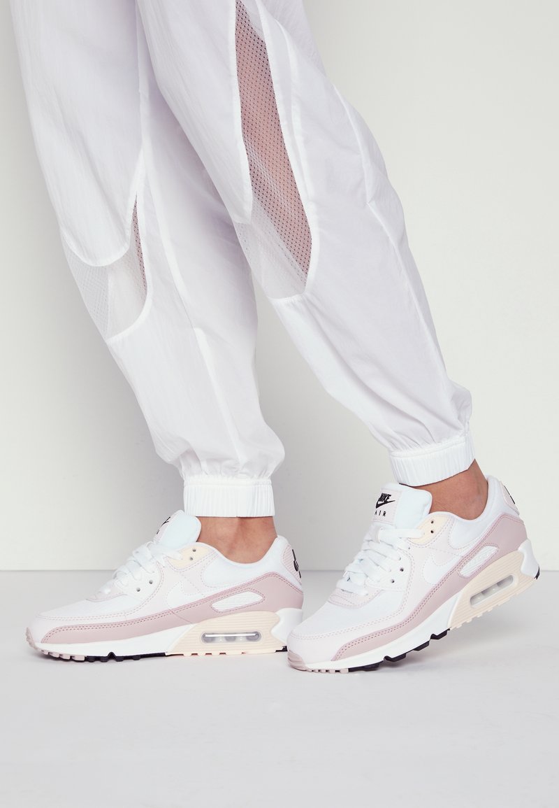 Witte en lichtroze Nike Air Max 90 sneakers hebben een bovenwerk van mesh, een gepolsterde kraag, zichtbare luchtkussen en een zwarte rubberen buitenzool.