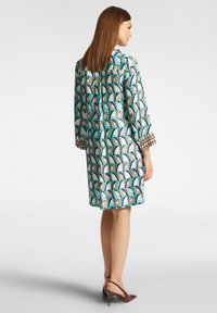 Vestito stampato in seta con design geometrici blu e marroni, maniche a tre quarti e dettagli decorativi sui polsini.