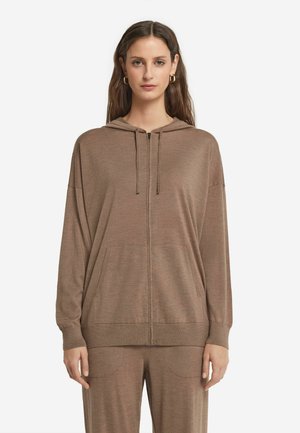Brauner Zip-Hoodie mit weicher Textur, übergroßer Passform, Fronttaschen und Kapuze mit Kordelzug. Kombiniert mit passenden braunen Hosen.