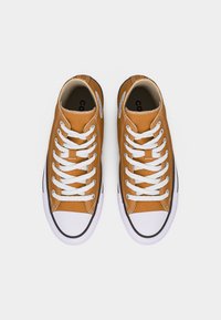 Ζευγάρι καφέ πάνινων παπουτσιών χαμηλής κορυφής με λευκές λαστιχένιες άκρες, λευκά κορδόνια και μαύρο περβάζι, σε θέα από πάνω πάνω σε λευκό φόντο.