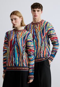 Des sweatshirts tricotés colorés avec des motifs abstraits ondulés en rouge, bleu, jaune et vert, dotés de poignets côtelés et d'un col rond.