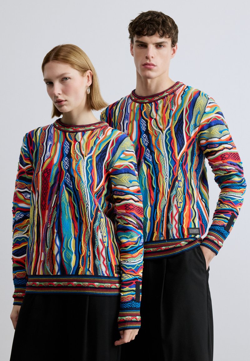 Des sweatshirts tricotés colorés avec des motifs abstraits ondulés en rouge, bleu, jaune et vert, dotés de poignets côtelés et d'un col rond.