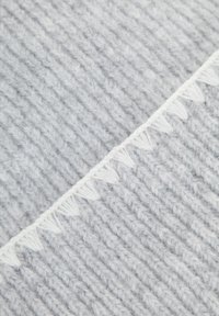 Tkaná deka v světle šedé barvě s žebrovanou strukturou, měkkou přízí a dekorativním bílým třásněm podél jednoho okraje.