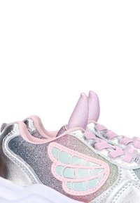 Zapatillas plateadas con detalles de cordones rosas y un diseño texturizado en forma de ala en el lateral. Presentan un material brillante e iridiscente y una lengüeta de malla.
