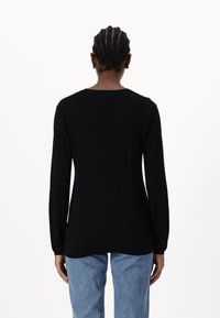 Black long-sleeve top with a round neckline, made from a smooth fabric, features a relaxed fit and side seams, paired with light blue jeans.