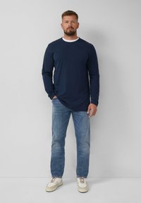 Marineblauwe longsleeve shirt met een ronde hals, gedragen met lichtblauwe jeans en beige sneakers. Eenvoudig ontwerp, zachte textuur, standaard pasvorm.