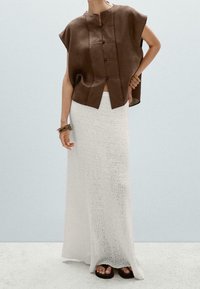 Top marrone in lino a maniche corte con bottoni sul davanti, abbinato a una lunga gonna bianca in maglia strutturata e sandali neri piatti. Design semplice e contemporaneo.