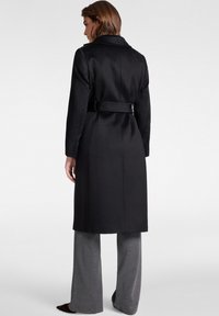 Trench nero con vita incinturata, design monopetto, colletto a lancia e maniche lunghe. Realizzato in tessuto liscio con una vestibilità sartoriale.