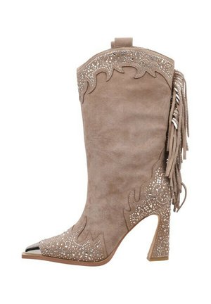 Botte de cowboy en daim beige avec un bout pointu, des franges décoratives, des découpes et des embellissements métalliques sur le côté.