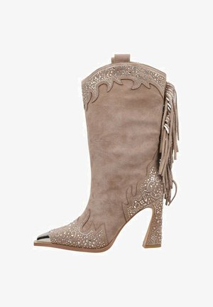 Bota de cowboy de ante beige con punta afilada, detalles de flecos, recortes decorativos y embellishments metálicos en el lateral.