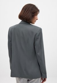 Mørkegrå blazer med en skræddersyet pasform, glat tekstur, skarpe revers og subtil skulderpuder, der har en rygventil for nem bevægelse.