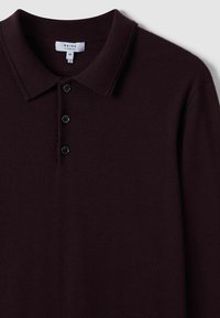Polo shirt a maglia borgogna, con colletto classico, patta con tre bottoni e texture liscia. Etichetta con la scritta "REISS," taglia media.