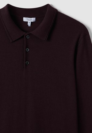 Polo de punto burdeos, con un cuello clásico, tapeta de tres botones y textura suave. La etiqueta dice "REISS", talla mediana.