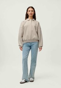 Ανοικτό γκρι πουλόβερ με γιακά, oversized στυλ και πλεκτές μανσέτες, συνδυασμένο με ανοιχτούς μπλε φαρδείς τζιν και καθημερινά αθλητικά παπούτσια.