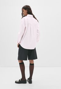 Lichtroze gestreept shirt met een losse pasvorm, voorzien van een puntige kraag en lange mouwen, gecombineerd met donkere gestreepte shorts en zwarte accessoires.