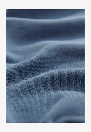 Material moale, de culoare albastră, cu un model texturat și striat. Țesătura pare ușoară și ușor șifonată, evidențiind pliabilitatea acesteia.